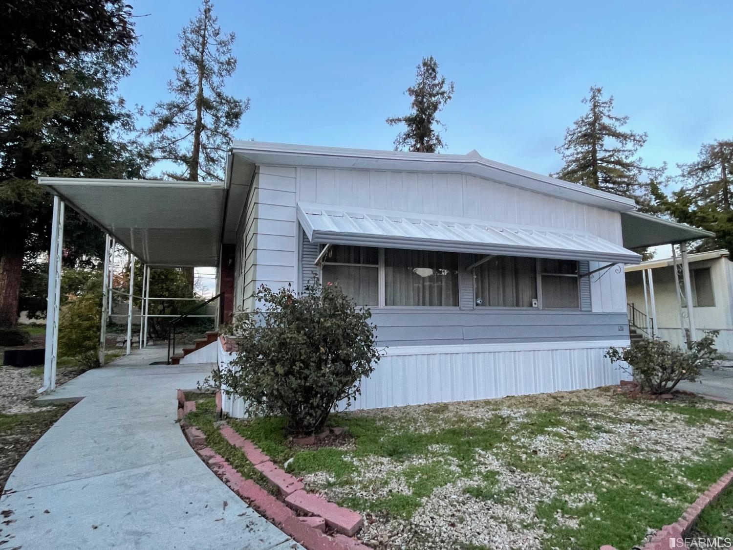 1421 Jerez Court Hayward, California Affordable, double wide manufactured home in an all ages park. The home features a spacious living room that flows to the dining room with built in buffet and cabinet. The kitchen features a dishwasher, gas stove top, double sinks, microwave and bonus desk built in wrapped at the end of the counter into the second living room. The remodeled Jack and Jill hallway bathroom connects to the second bedroom, perfect for a home office or guest room. The large primary bedroom is at the back of the hallway with three closets and bonus vanity counter with mirror in the bedroom. The en suite bathroom is remodeled and updated with beautiful tile, sink and plumbing fixtures. The side-by-side washer and dryer with storage in the laundry room leads to the side door to the covered parking spaces and storage shed. The outdoor area wraps around both sides of the home and is riddled with large, mature redwood trees, a fruiting lemon tree and plenty of room for a garden. This home is primed and ready for a new owner to make it their own.